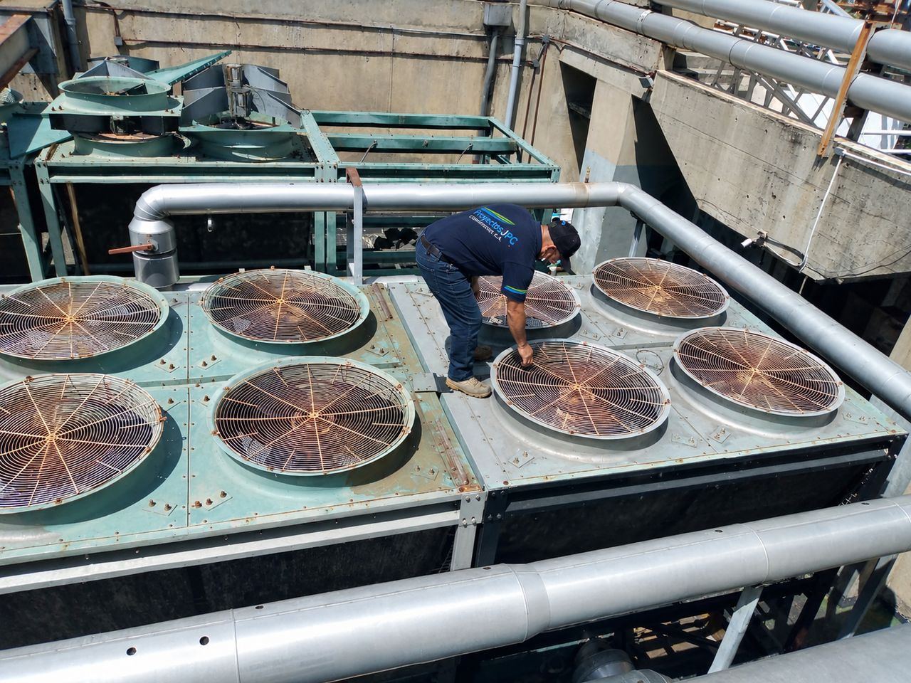 Técnico de Proyectos JPC revisando los ventiladores de un condensador de aire acondicionado en una azotea.