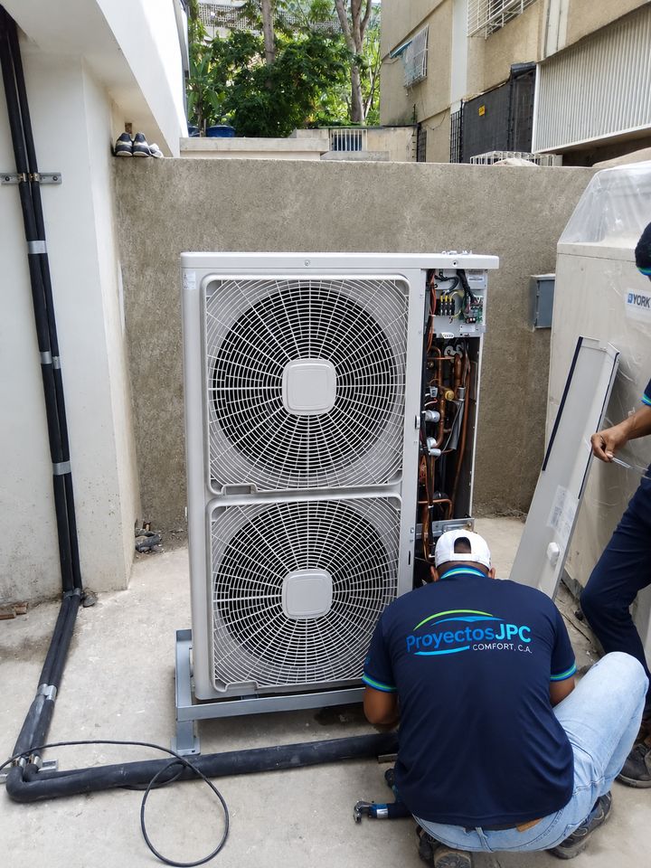 Técnico de Proyectos JPC, con el logo de la empresa en la camisa, instalando una unidad condensadora de aire acondicionado.