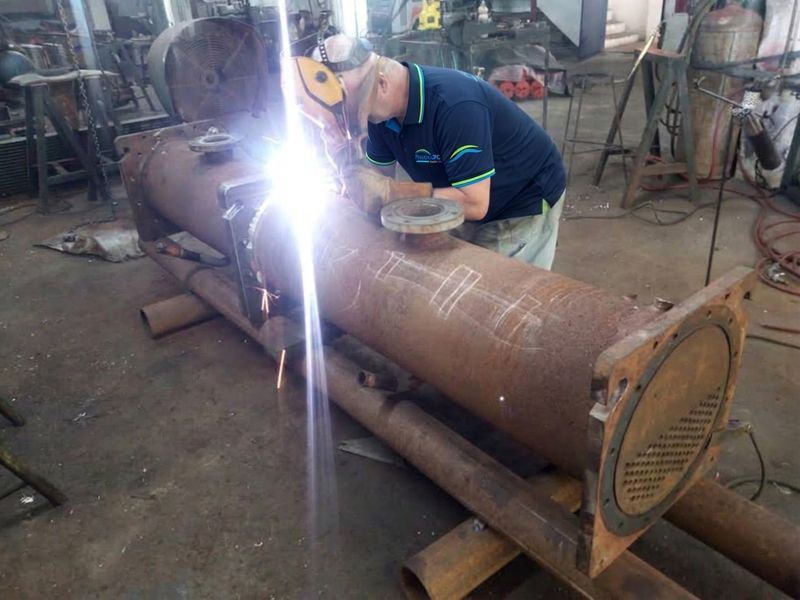 Técnico de Proyectos JPC con careta de soldar soldando un intercambiador de calor en un taller.